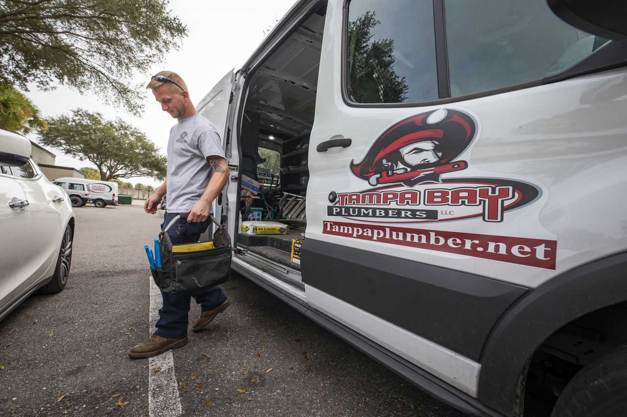 Tampa Bay Plumbers technician carrying a tool bag from a branded company van