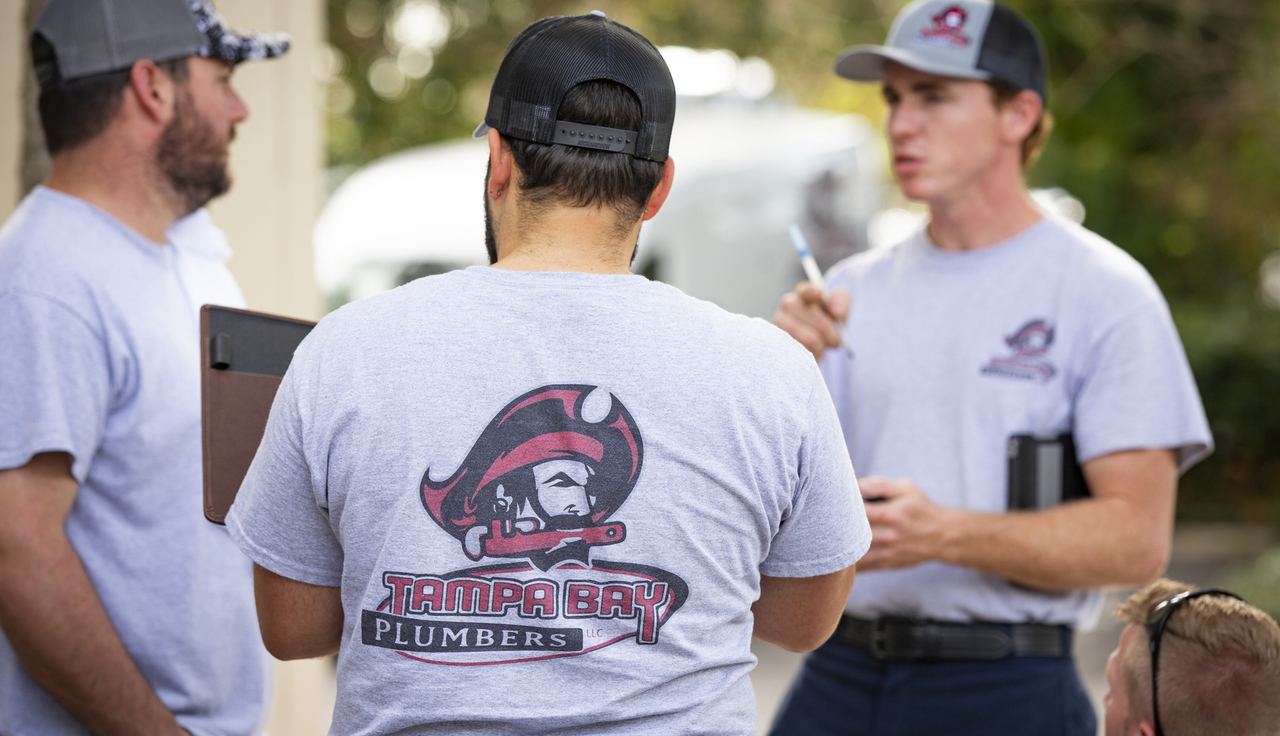 Three Tampa Bay Plumbers crew members in branded shirts talking through a job on site