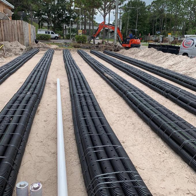 Large commercial drain field laid out in sand with an excavator on site