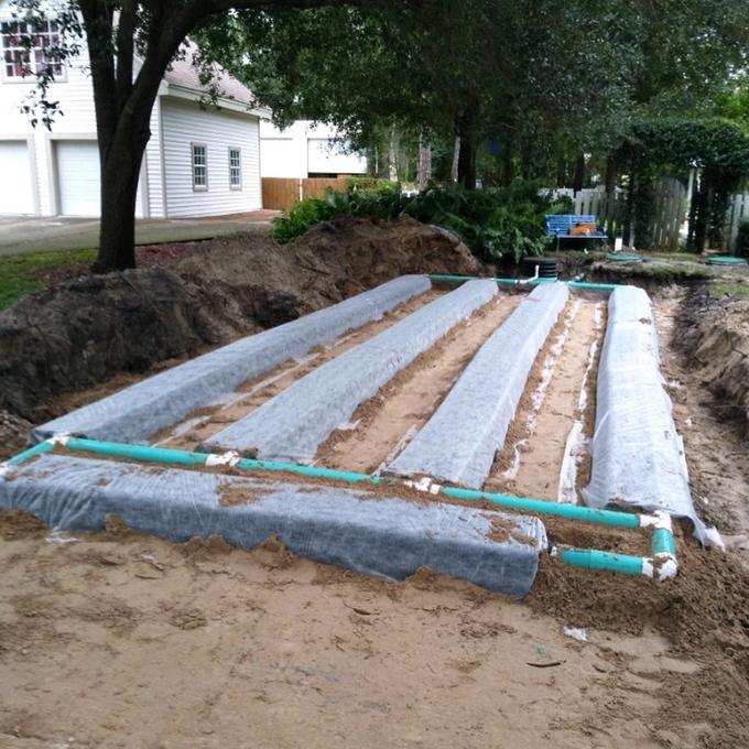 Completed residential drain field with wrapped laterals and green distribution lines ready for backfill