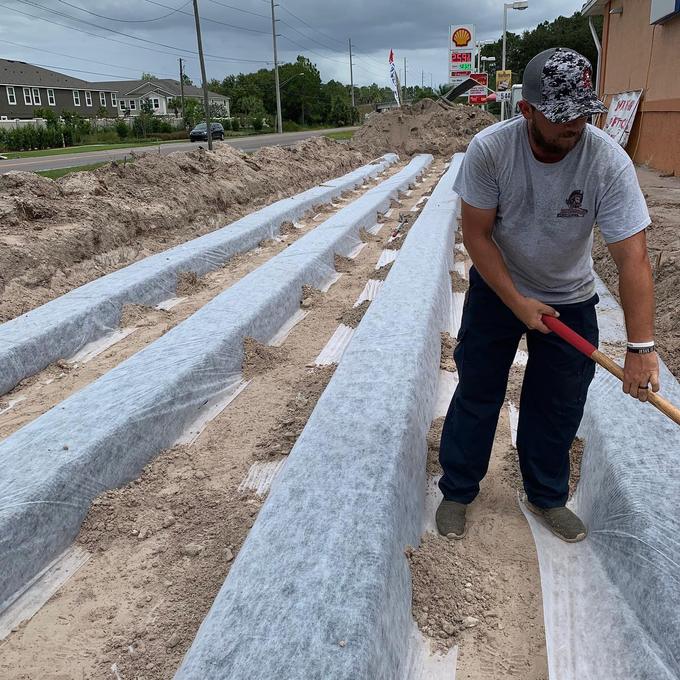 Tampa Bay Plumbers technician raking sand between wrapped drain field laterals on a commercial site