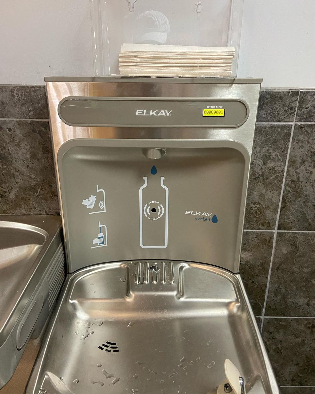 New stainless steel bottle filling station and drinking fountain installed on a tiled wall at a school