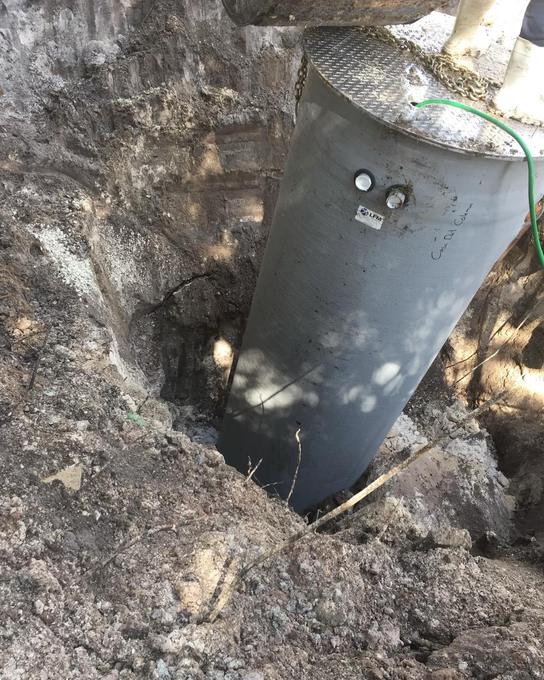 Concrete lift station wet well being lowered into an excavation with a steel access lid fitted