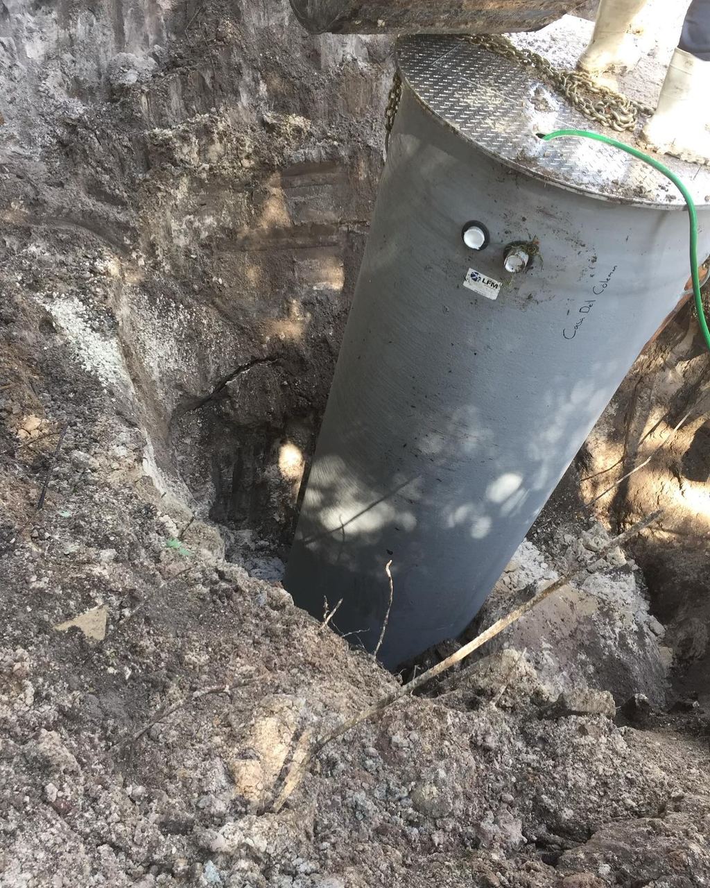 Concrete lift station wet well being lowered into an excavation with a steel access lid fitted