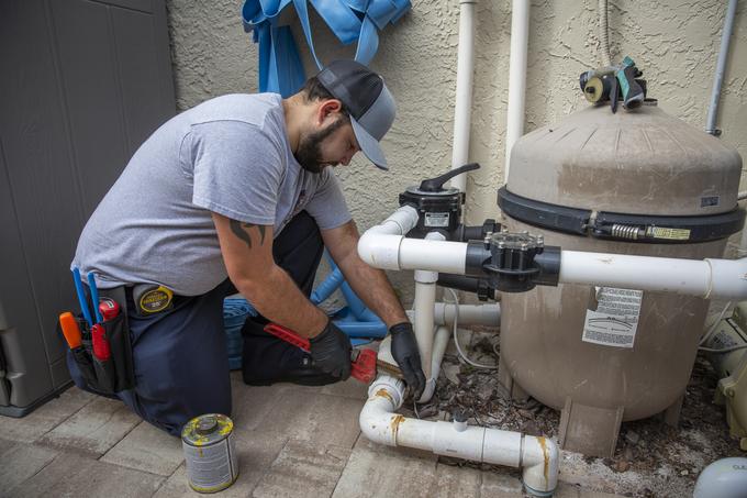 Tampa Bay Plumbers technician gluing PVC pipework at a tank style filter unit outside a Tampa home
