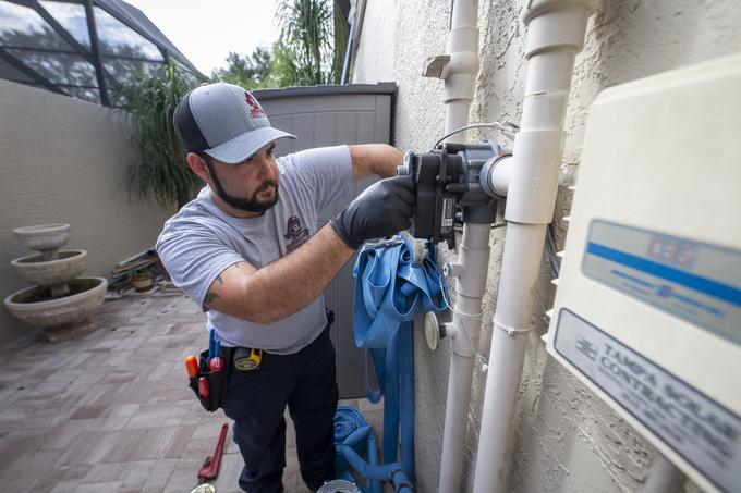 Technician servicing an outdoor valve assembly mounted on PVC against the exterior wall of a Tampa home