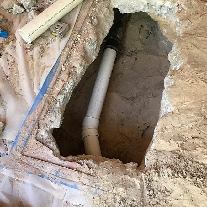 Concrete patio broken open to expose a repaired drain line joined with a new PVC section and coupling