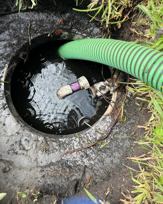 Suction hose lowered into an open septic tank with the liquid level visible inside