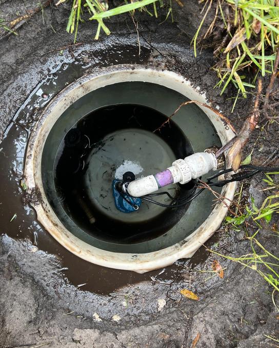 Open septic pump chamber showing a submersible pump, float switches and the discharge pipe
