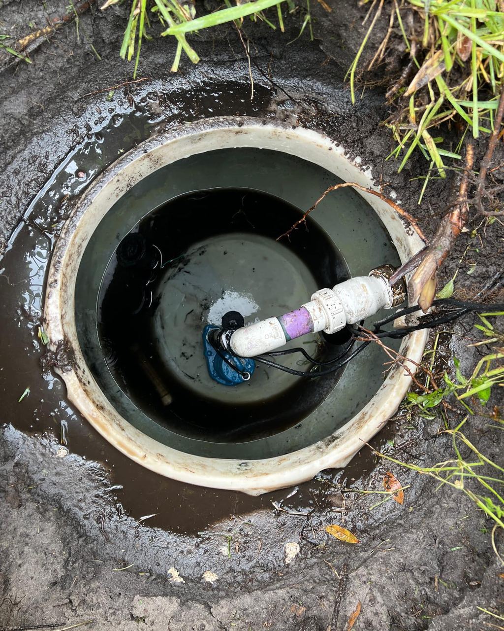 Open septic pump chamber showing a submersible pump, float switches and the discharge pipe