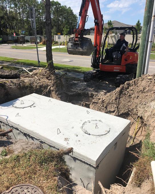 Precast 2,000 gallon concrete septic tank set into an excavation with a mini excavator working alongside