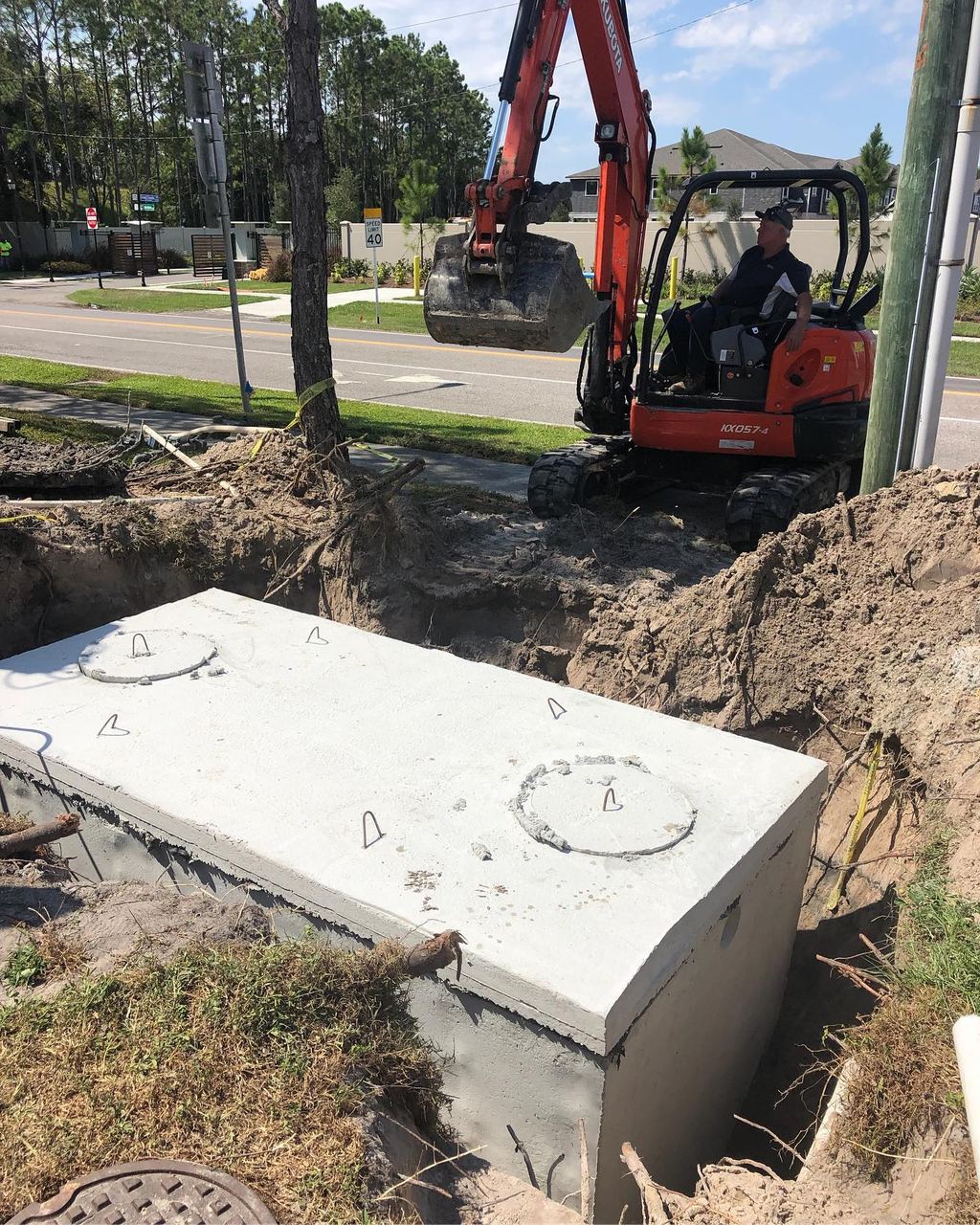 Precast 2,000 gallon concrete septic tank set into an excavation with a mini excavator working alongside