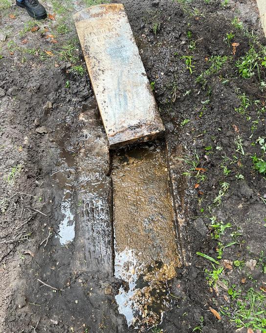 In-ground tank with the lid lifted clear, showing the channel and standing effluent before pumping