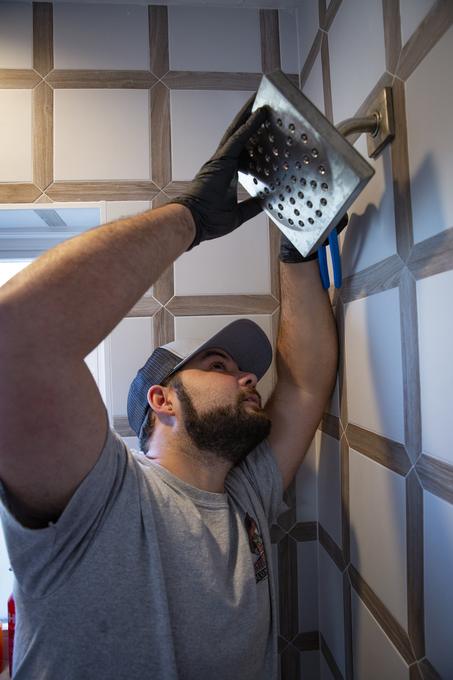Tampa Bay Plumbers technician fitting a square rain shower head to a tiled bathroom wall