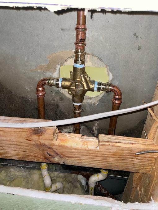 New brass shower mixing valve roughed in with copper risers through an opened block wall