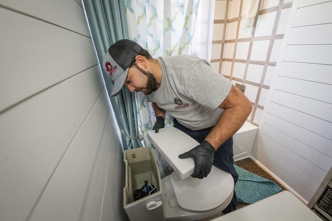Technician lifting the tank lid from a toilet during a repair in a Tampa bathroom