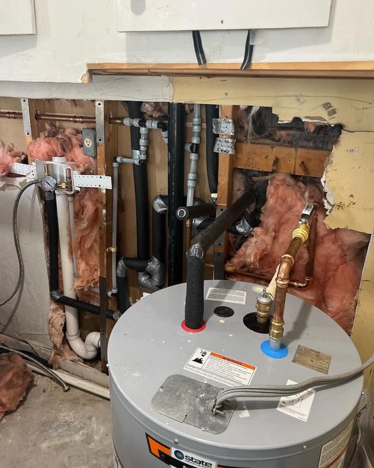 Electric water heater newly connected with copper flex lines and a pressure gauge in an opened utility wall