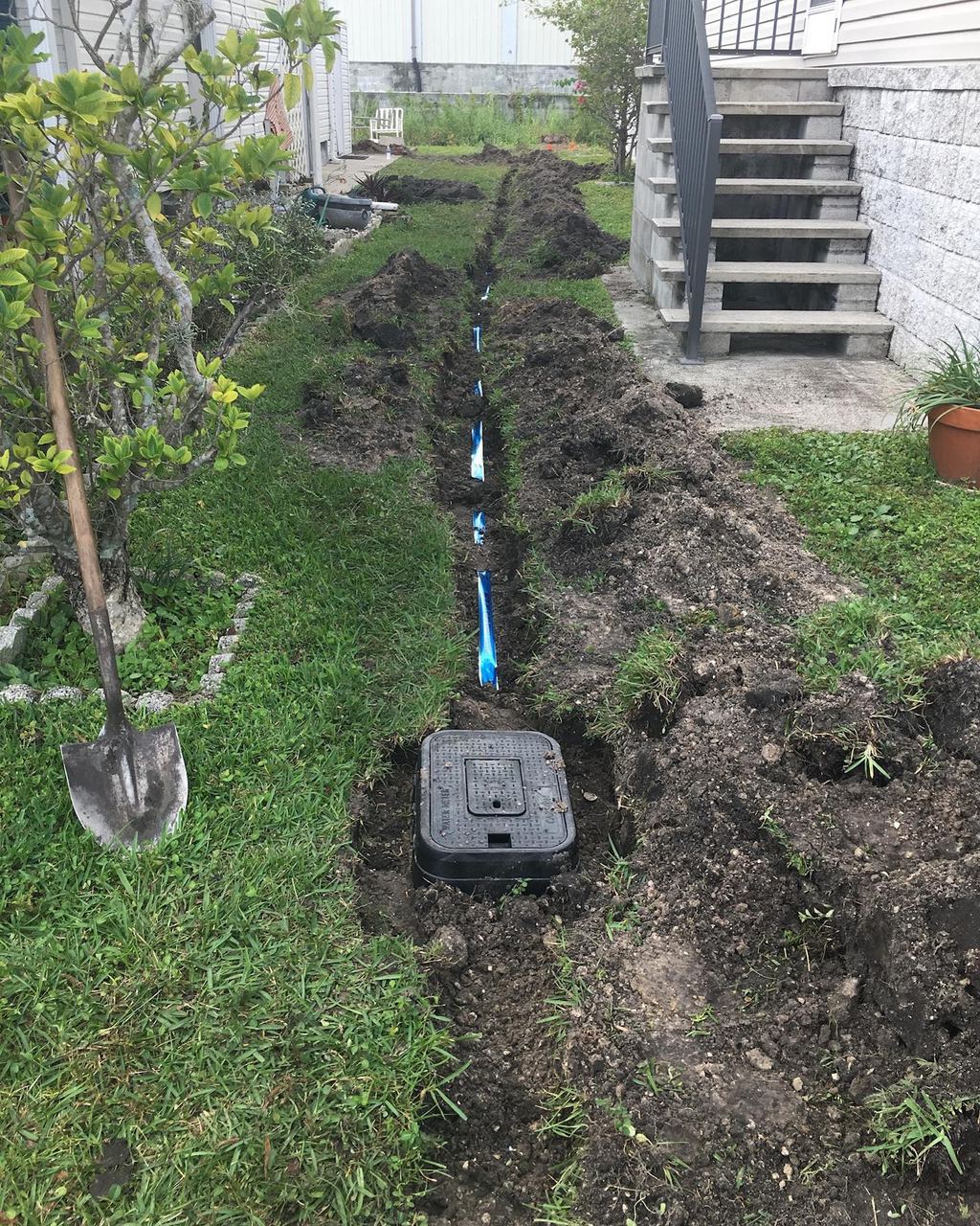 New blue polyethylene water service line laid in a trench along the side of a house with a new meter box installed